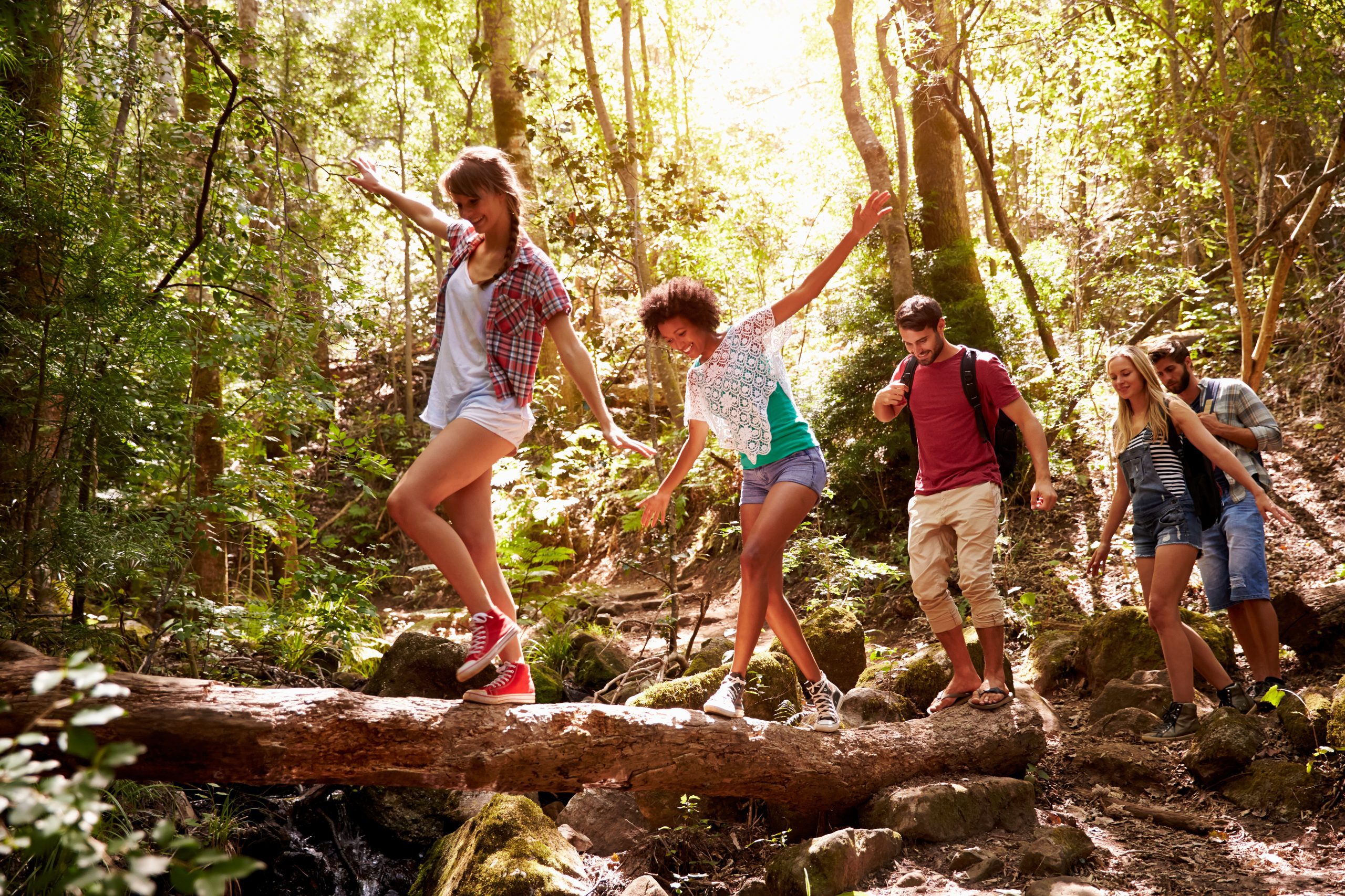 Four kids balancing on a large wooden log in a forest