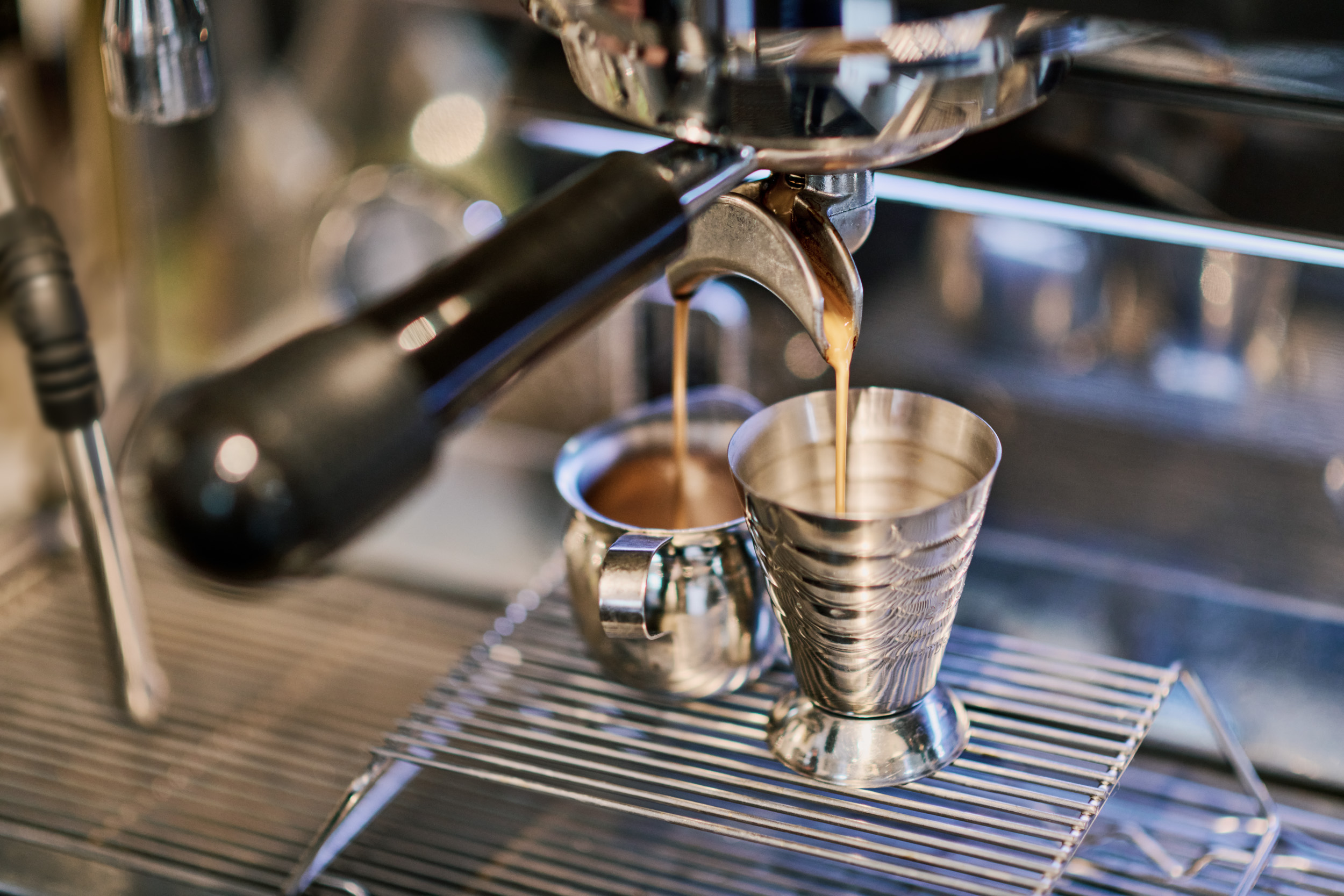 Espresso being poured into two metal cups.