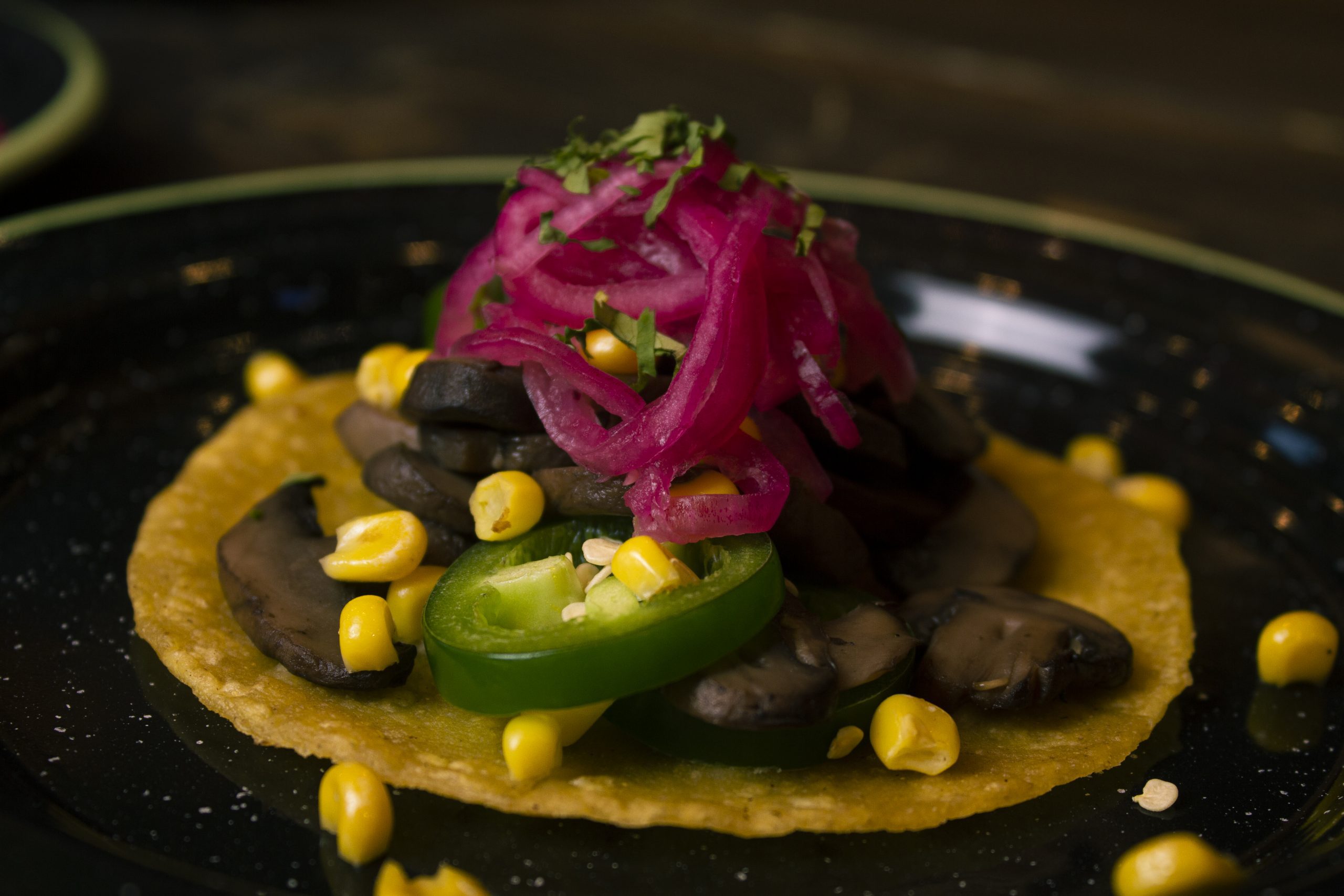 Close up of a single taco with corn, mushrooms and pickled onion.