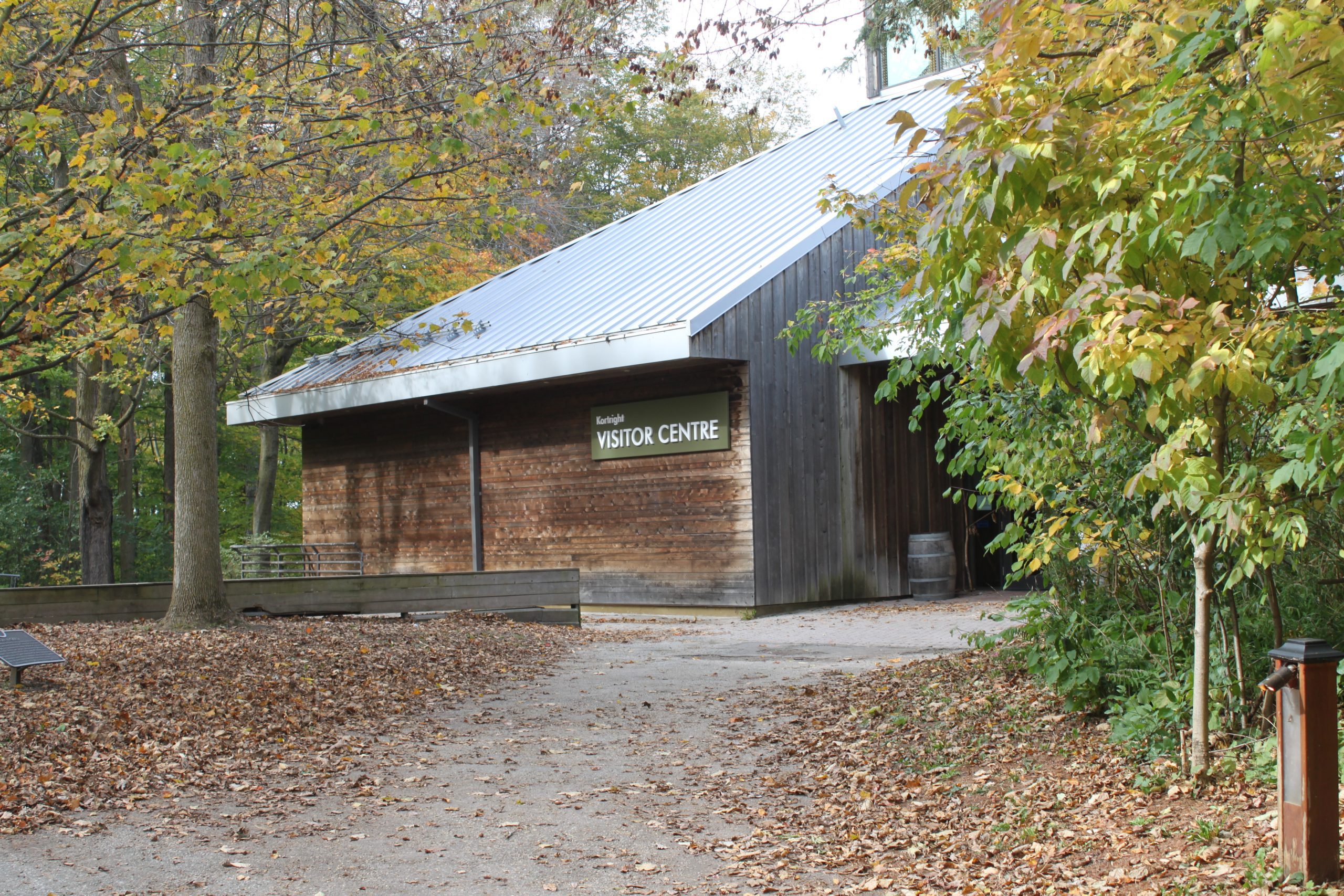A wood-sided building with the sign Visitor Centre sits among a forest with a paved path leading to it.