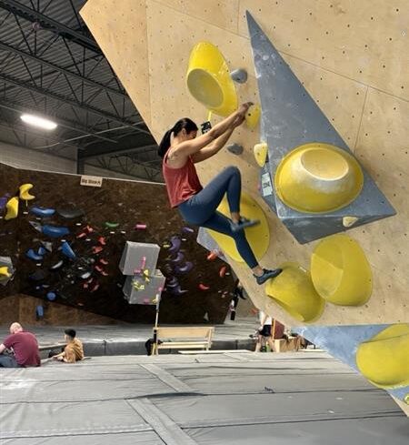 Image of a person at an indoor rock climbing gym, climbing up a wall