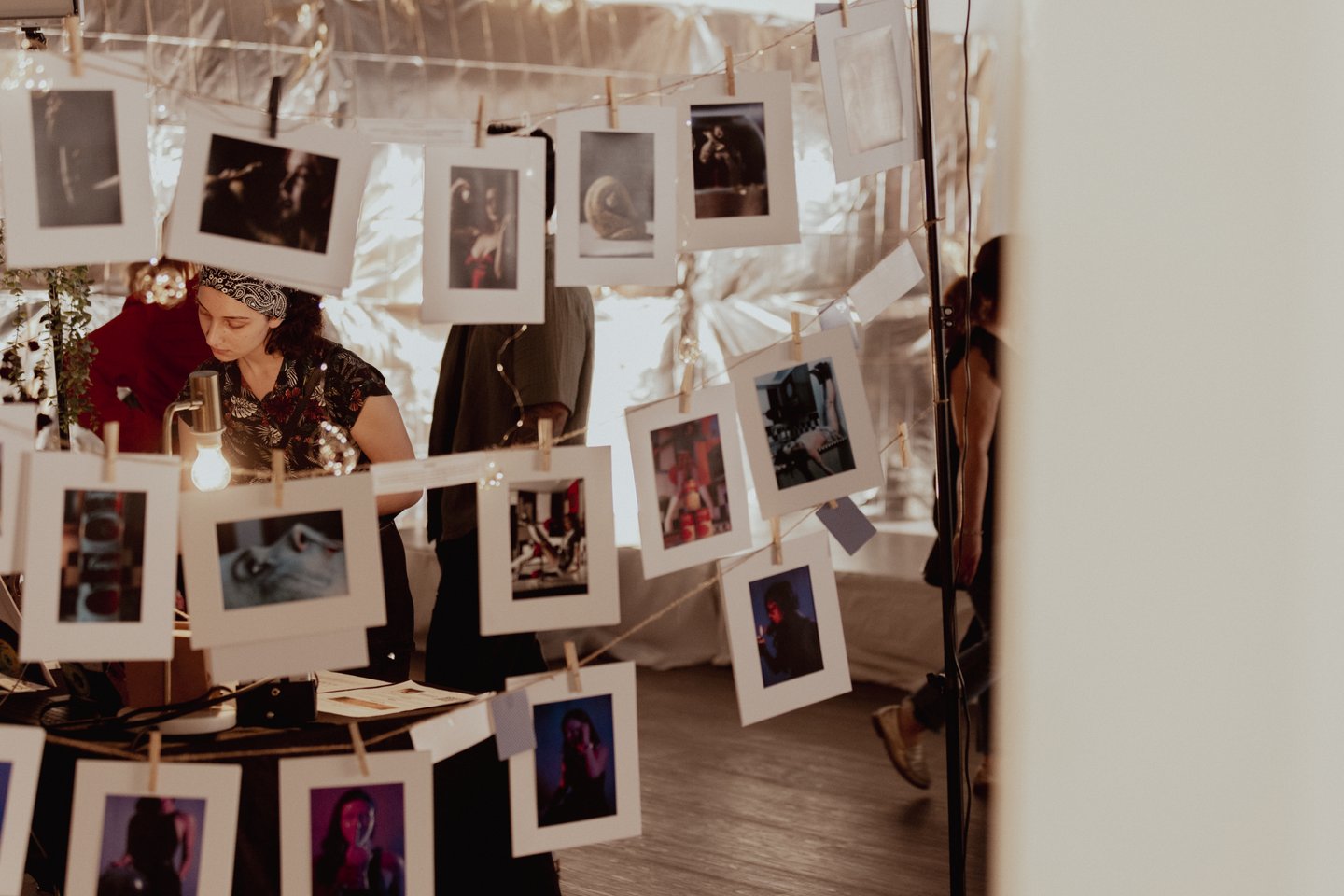 Polaroid photos hanging from a wire with a woman standing behind them, looking elsewhere.
