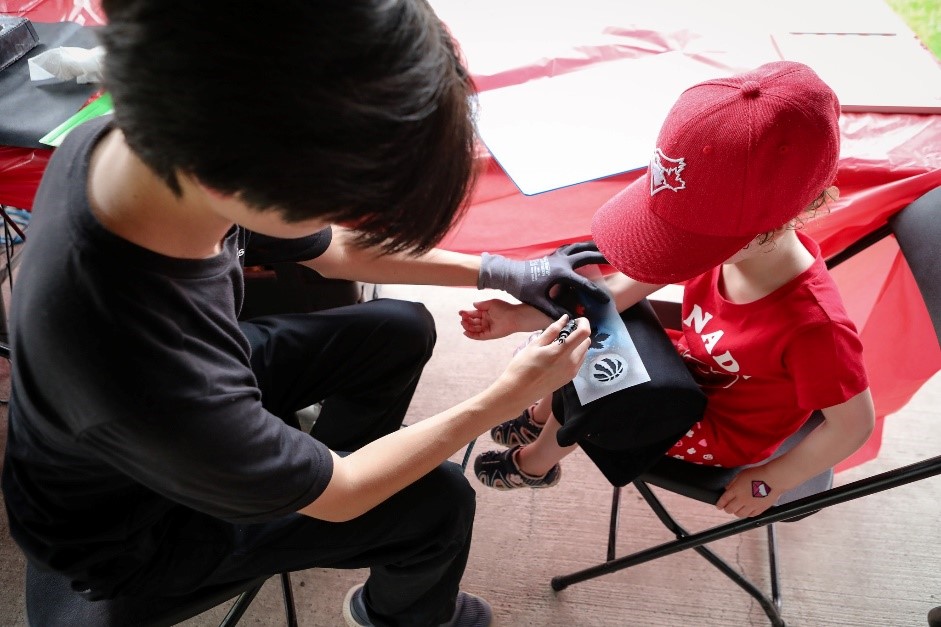 A temporary spray tattoo artist working on a child with red attire.