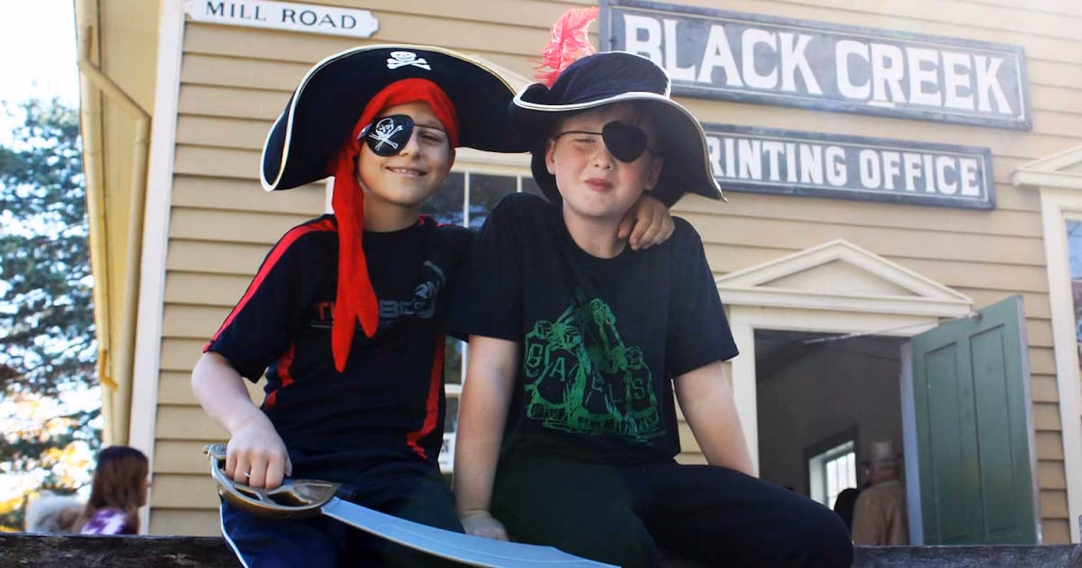 Two children dressed as pirates sitting in front of a Black Creek building