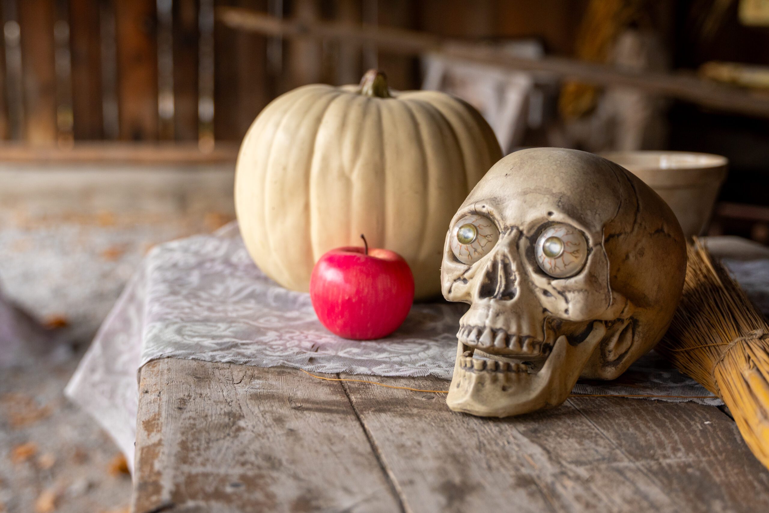 A pretend skull, white pumpkin and red apple positioned on top of a wooden table