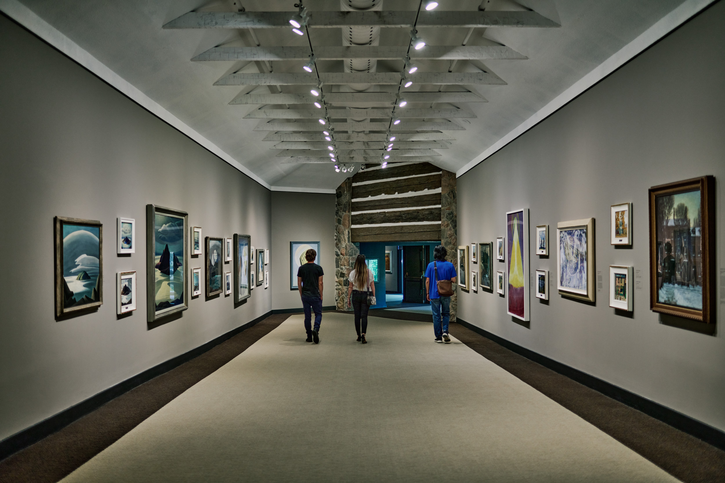 Three adults walking down the hallway of an art gallery, art lining the walls