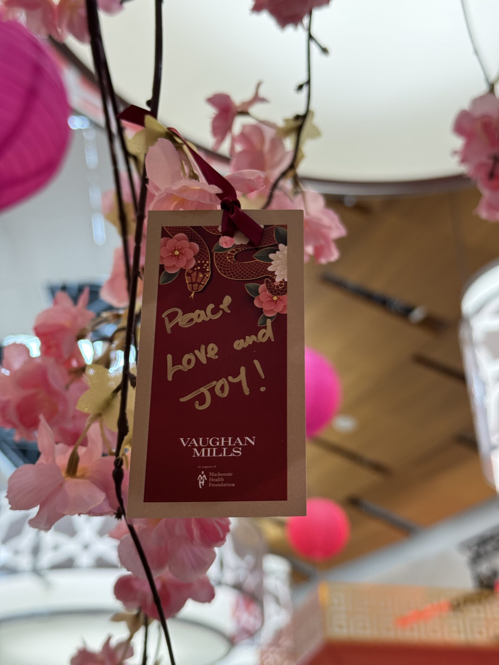 Image of a card hanging from a cherry blossom tree with warm Lunar New Year wishes written on it