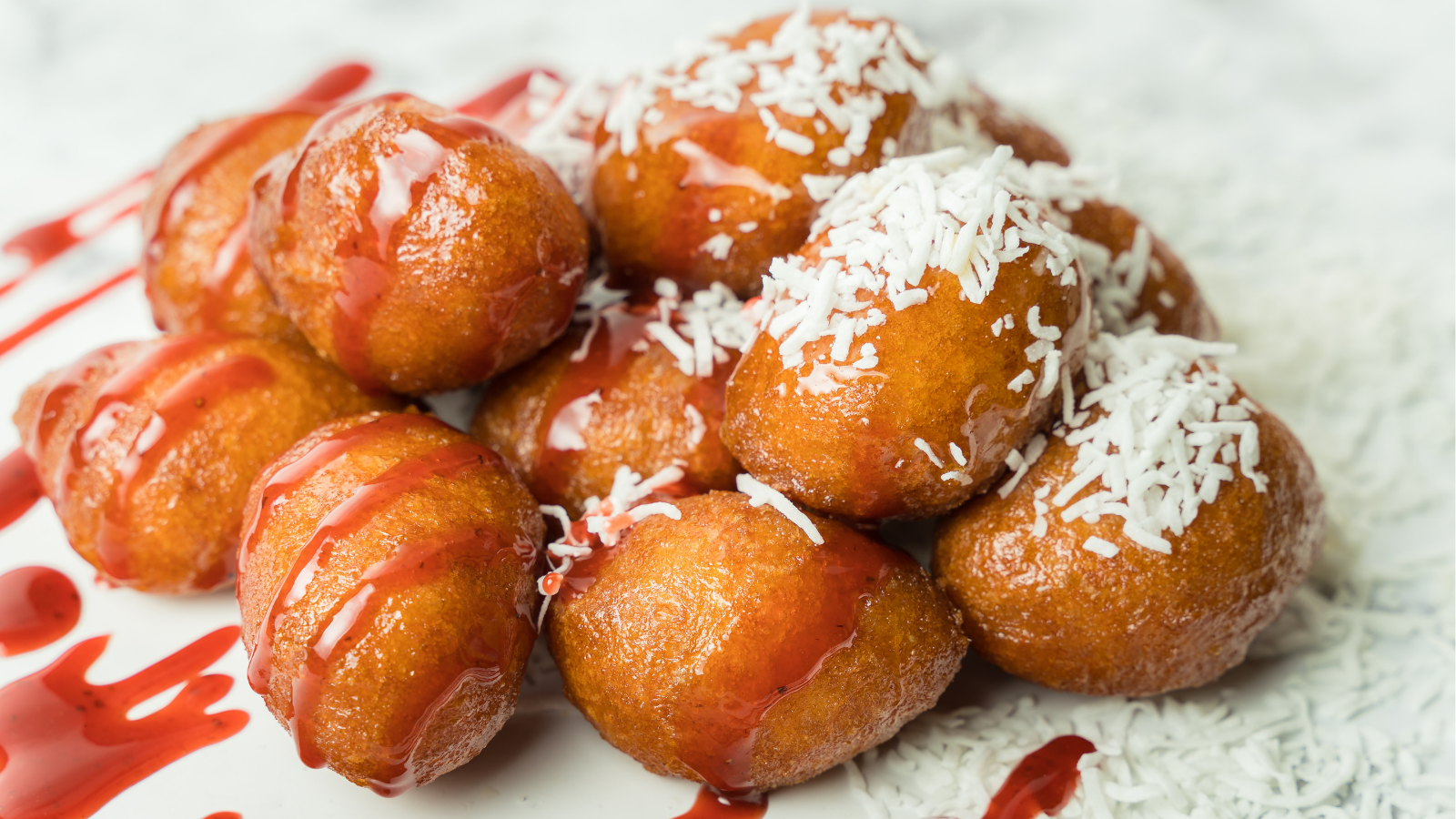 Image of fried dough balls with coconut and strawberry sauce on them