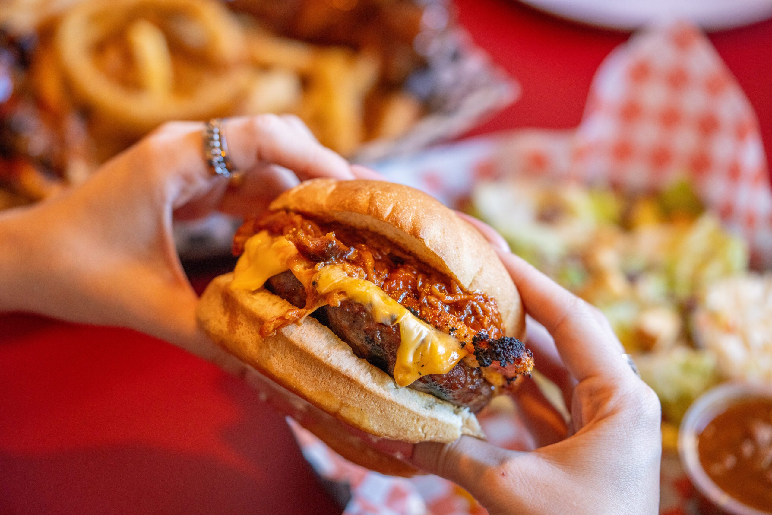 Aerial view of someone holding a cheeseburger in their hands, other dishes of food are blurry in the background