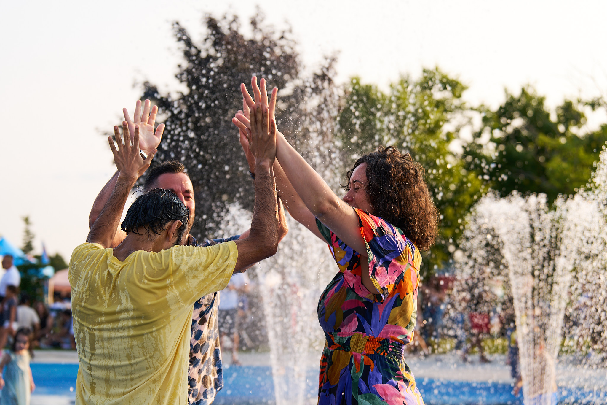 Three people high-fiving at a water park, sprinklers are going off in the background