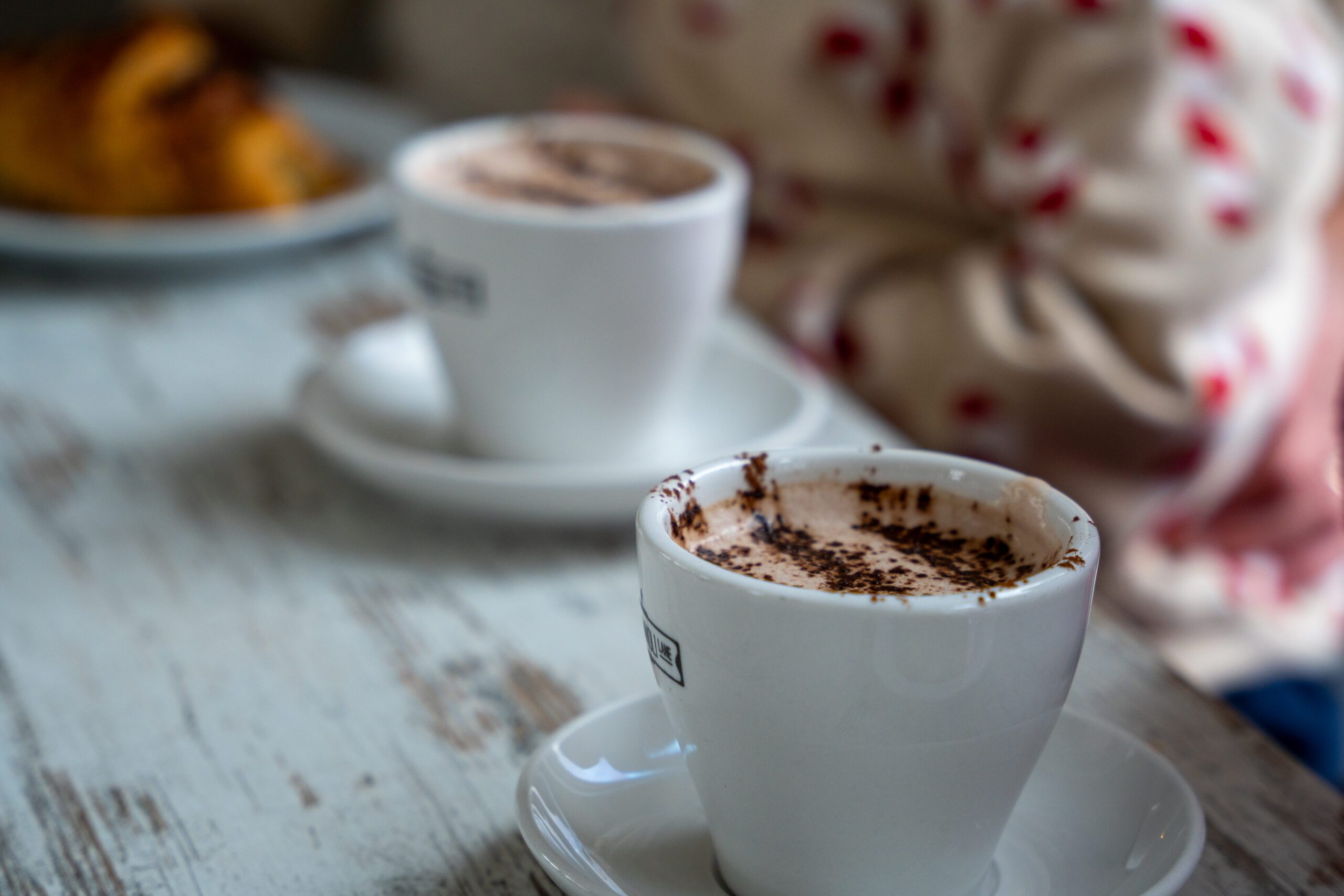 Image of two mugs of hot chocolate on a table with a person sitting behind them