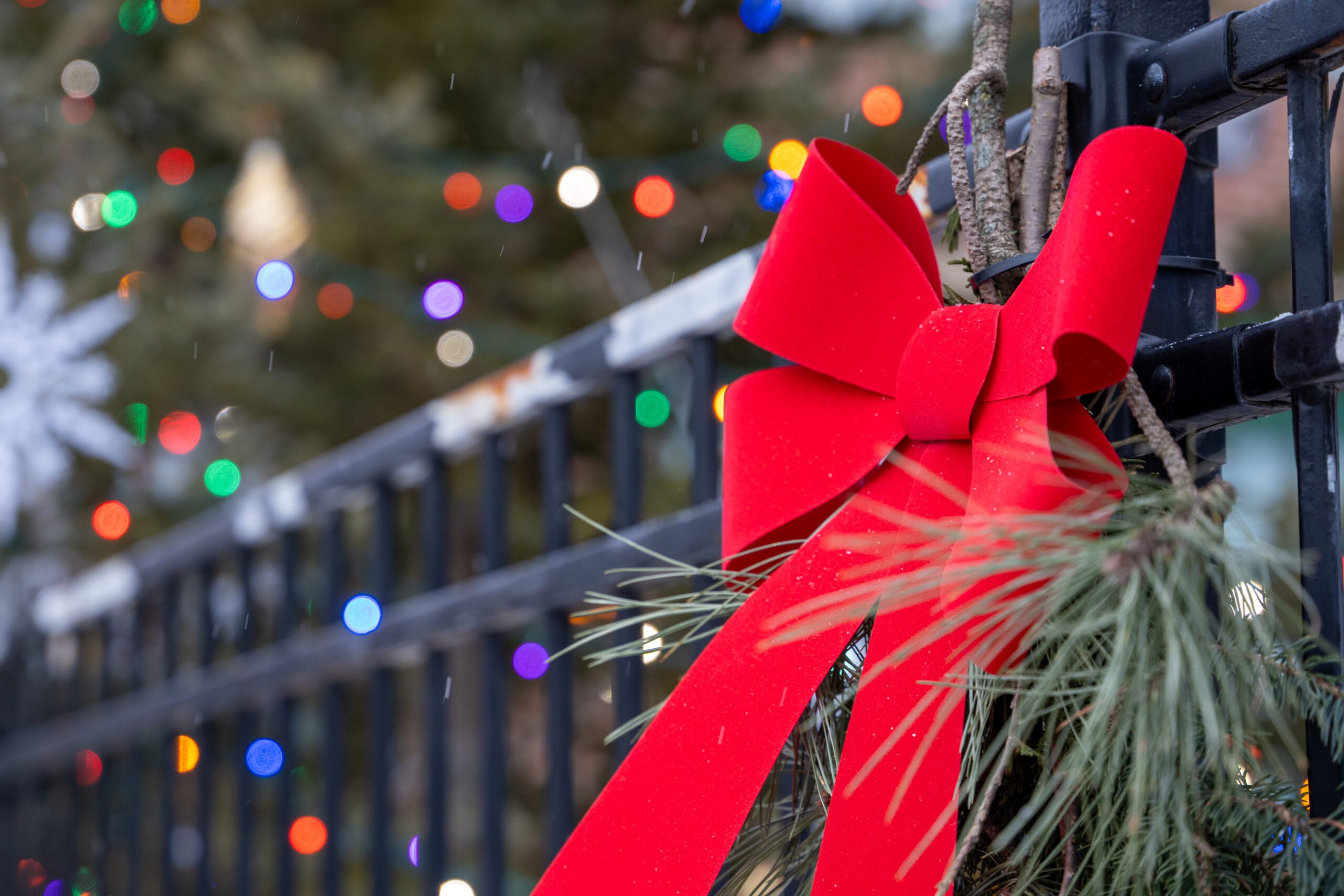 Image of a red bow on a fence with illuminated multicolour string lights out of focus in the background