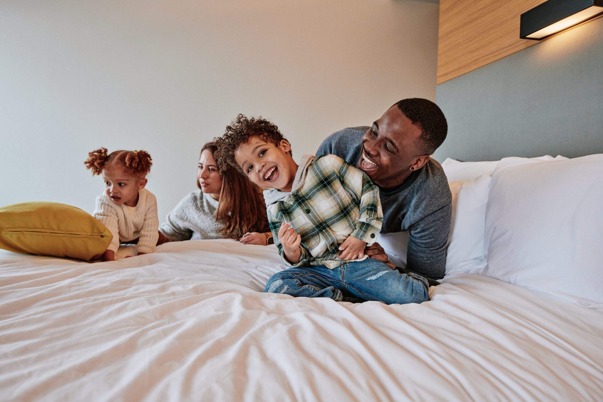 family playing on bed in hotel room, dad and son are laughing