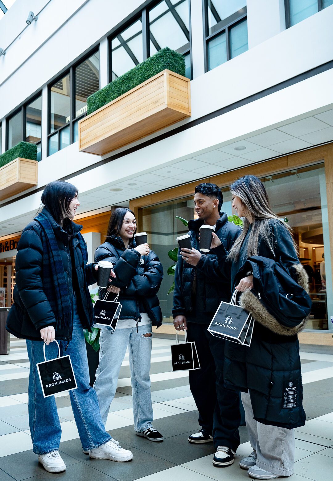 Four young adults standing in a mall drinking coffee and chatting while holding shopping bags