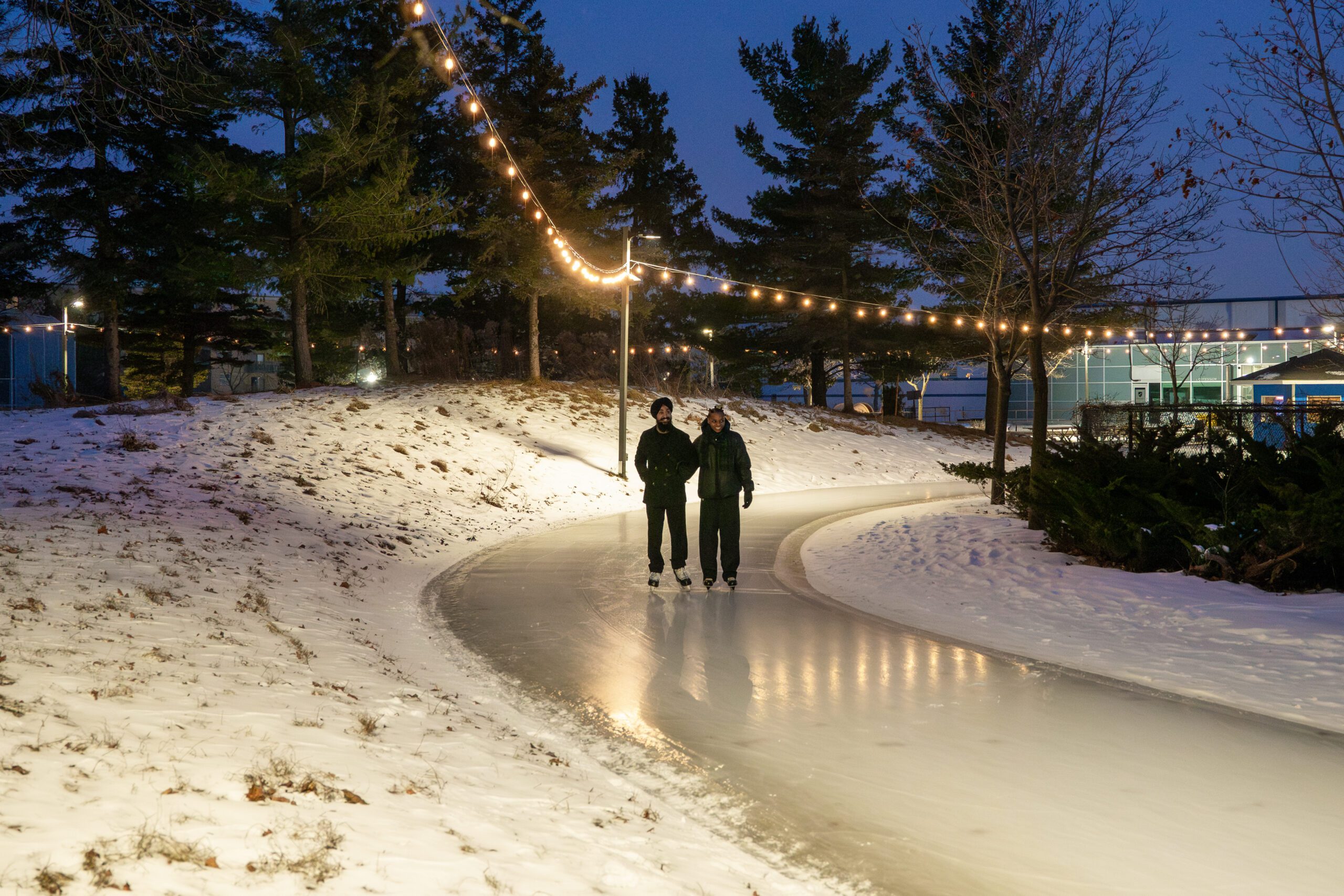 Image of two people skating on an outdoor skating trail under pretty string lights