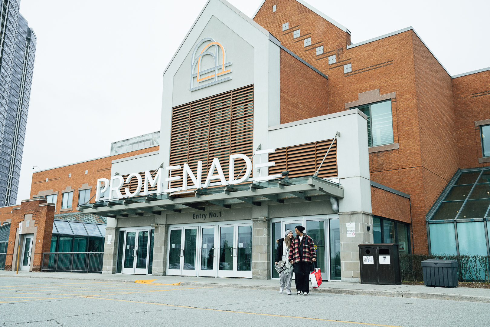 Image of two people walking out the doors of a shopping mall with bags in their hands.