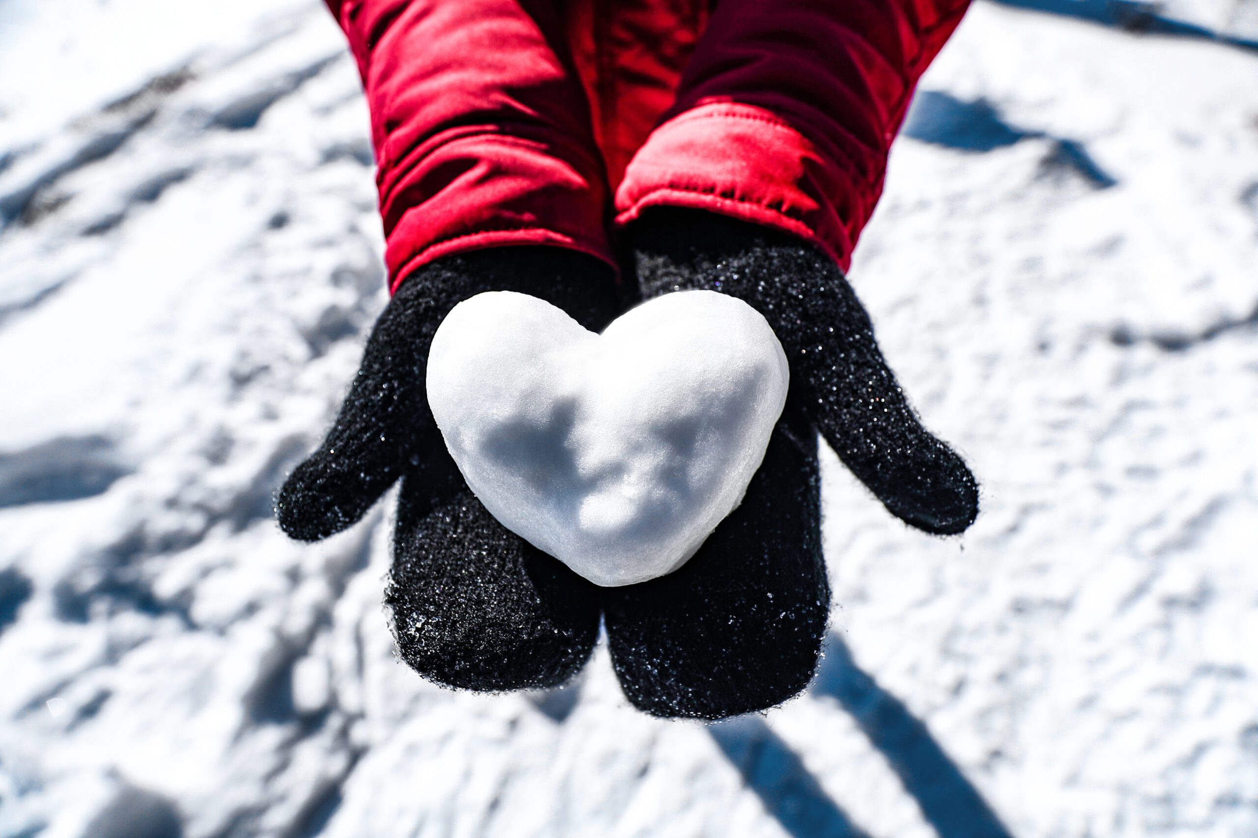 Image of a person holding out their hands with mittens on them holding a snowball in the shape of a heart