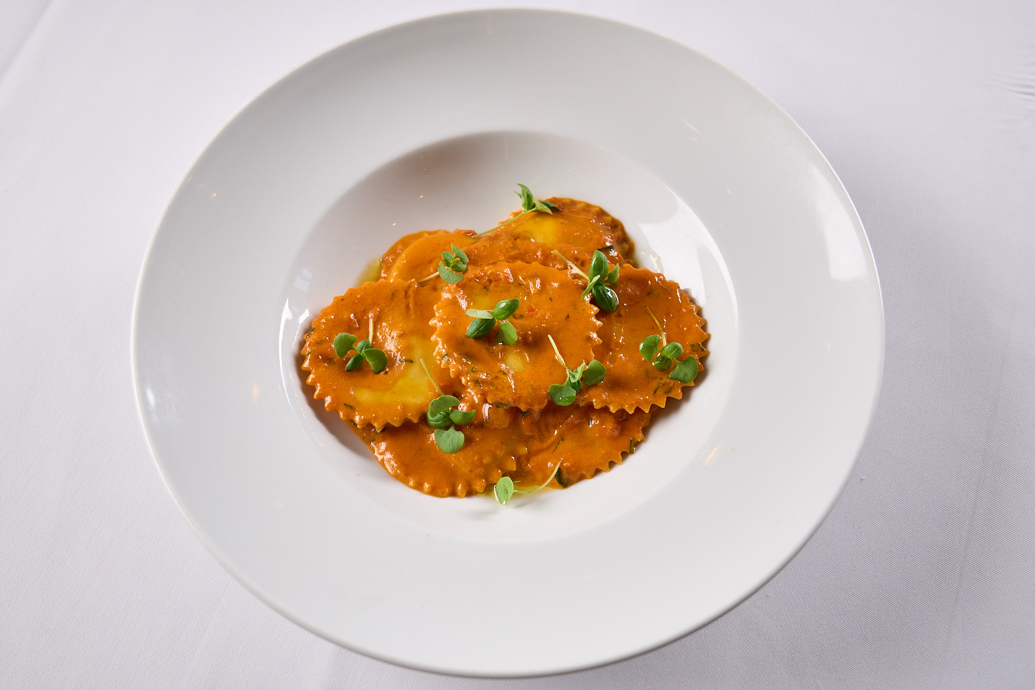 Image of a bowl of stuffed pasta in sauce with a green herb garnish