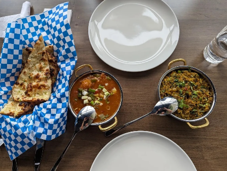 Image of bowls of curry and a basket of naan on a table at a restaurant