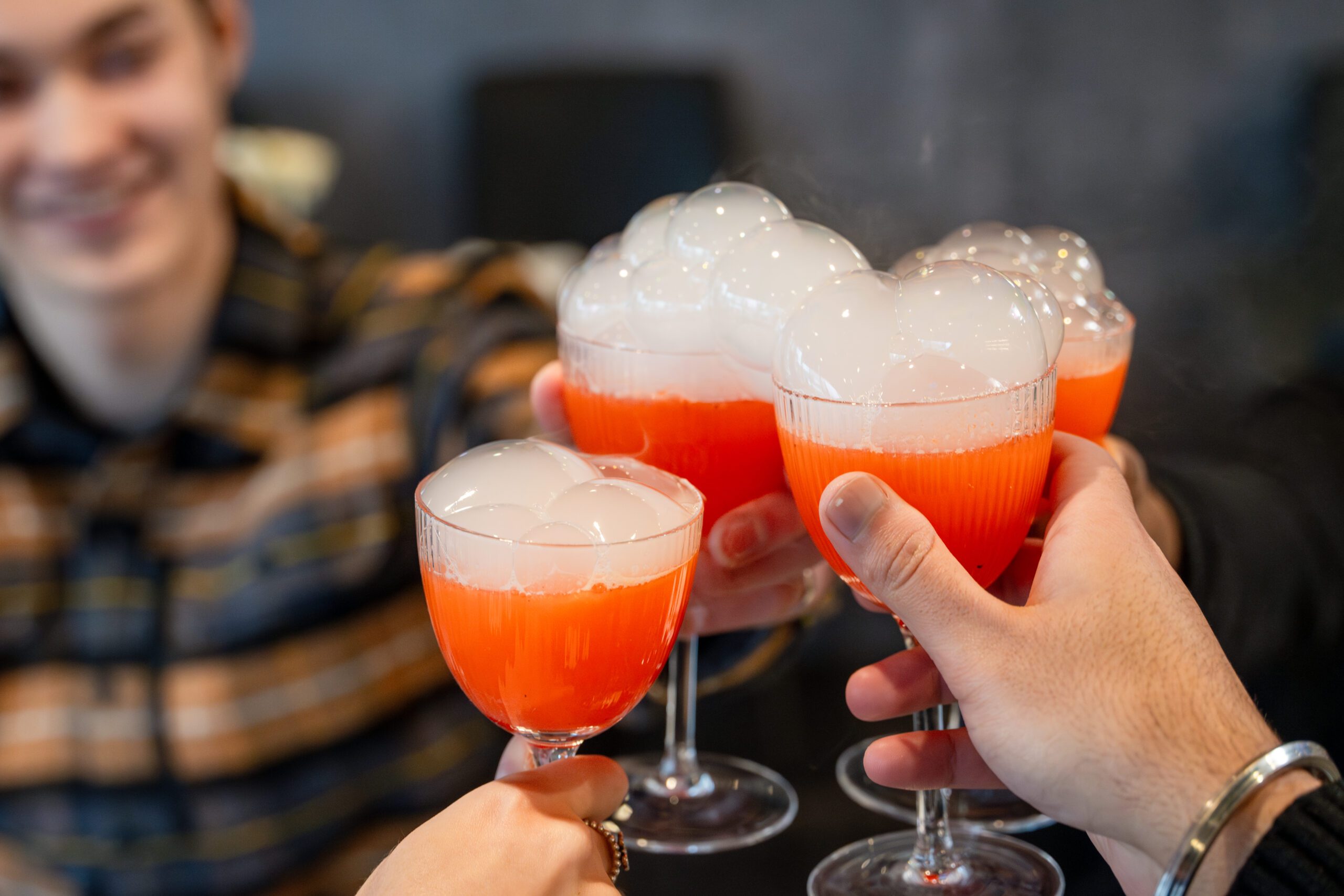 Image of people clinking glasses together full of a red cocktail with bubbly foam on top