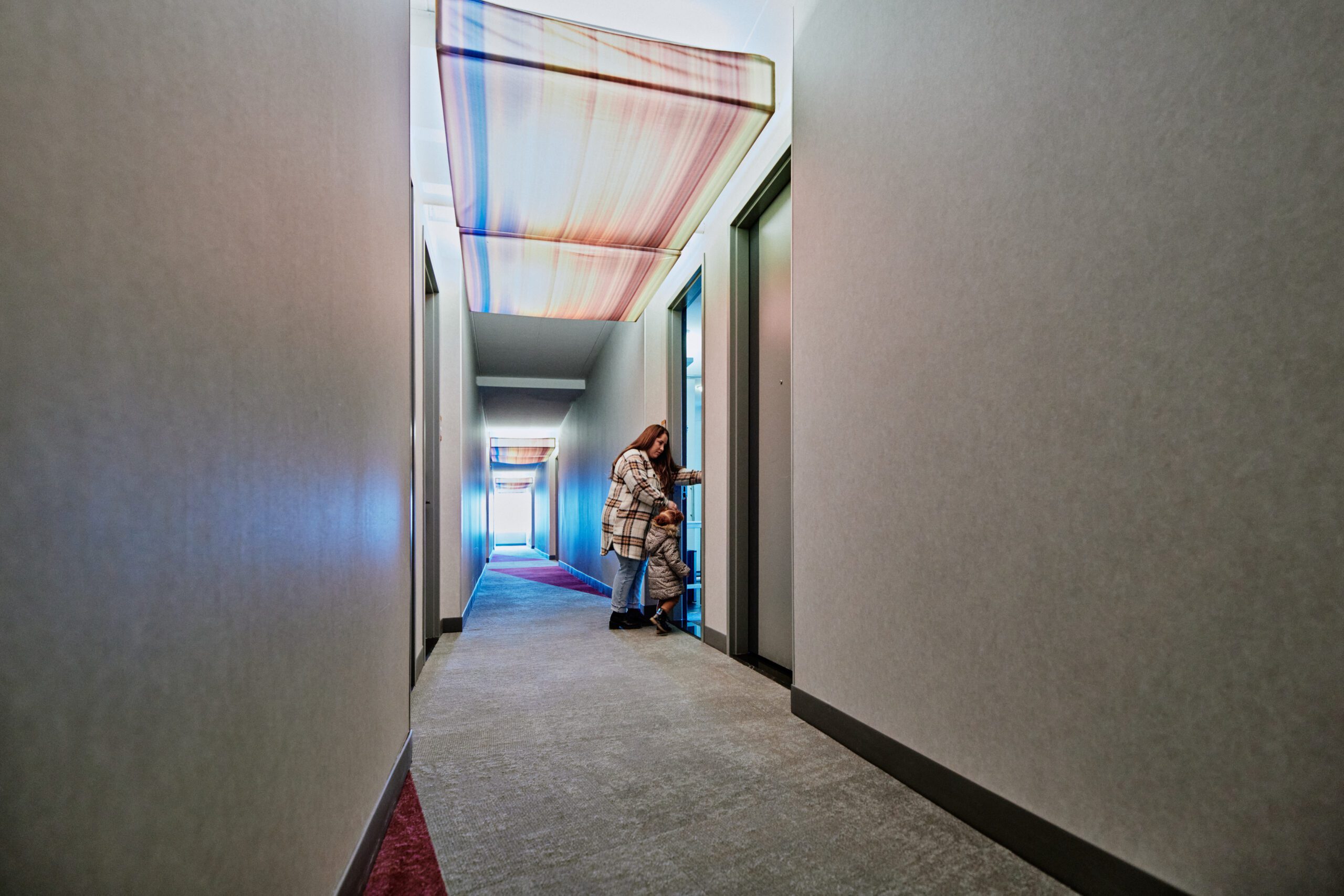 Image of a parent with their child standing in a hotel hallway opening the door to their room