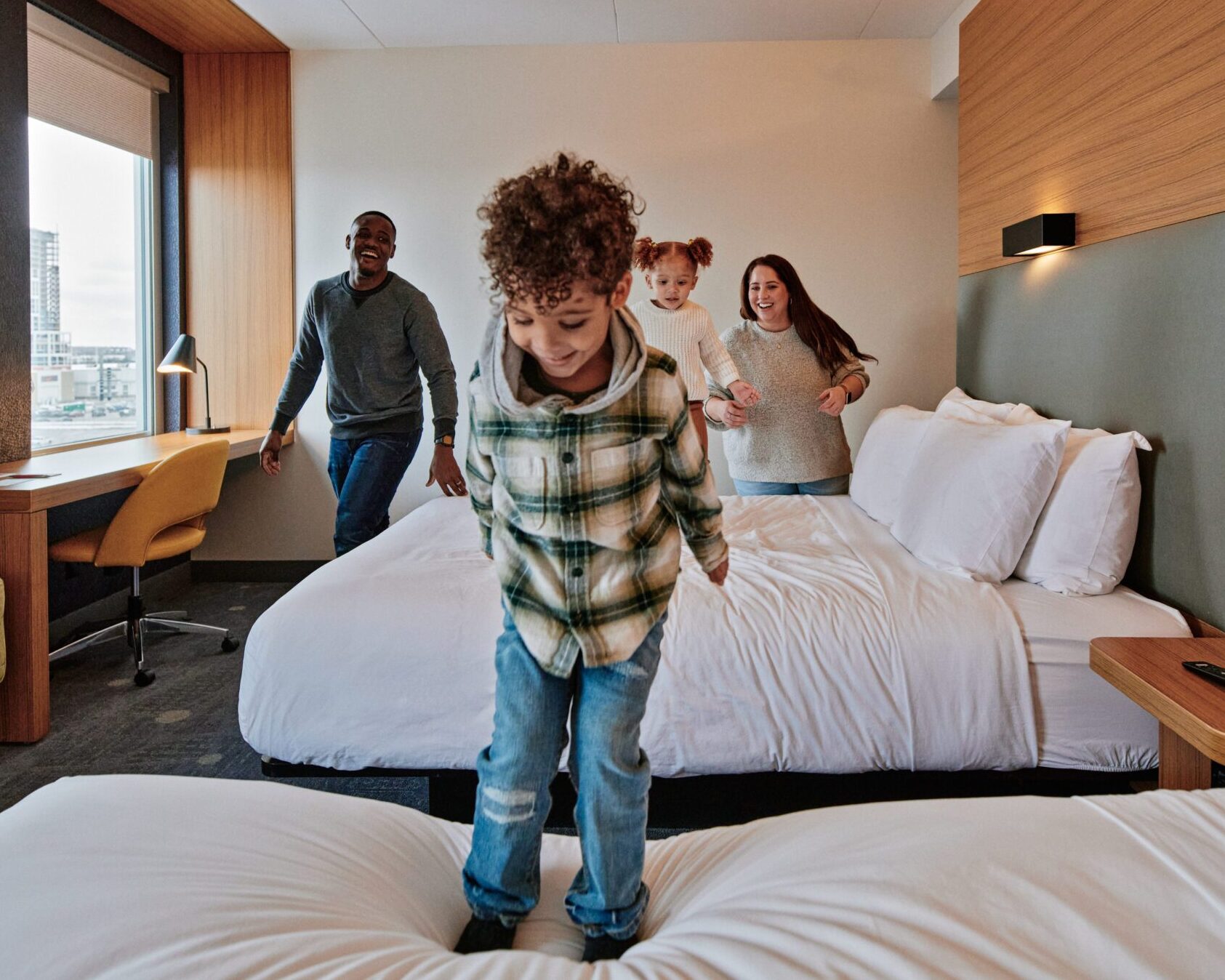 Image of a family in a hotel room and a child is jumping on the bed