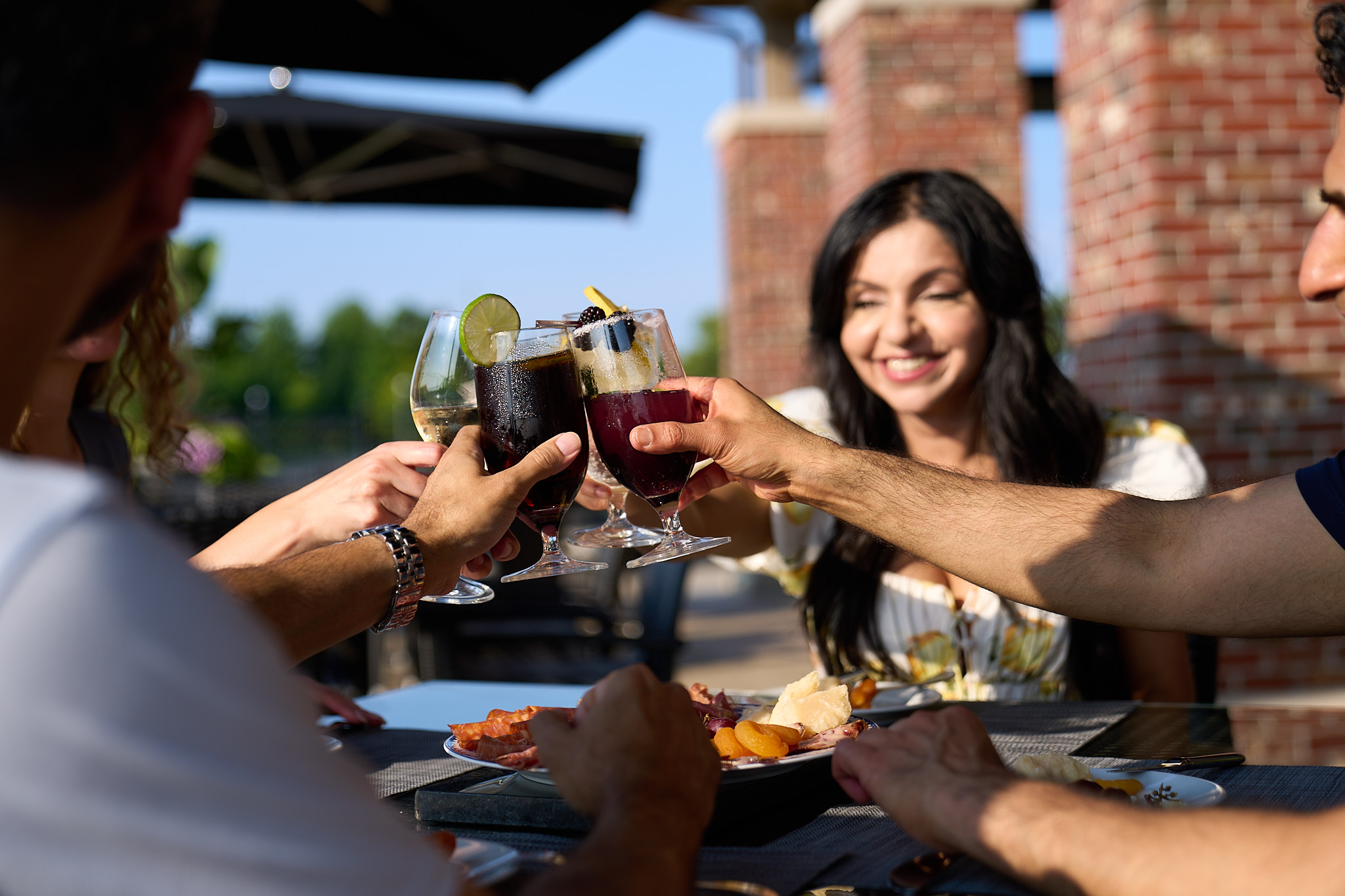 Image of four adults sitting on a restaurant patio and they are all holding their glasses in the air together.