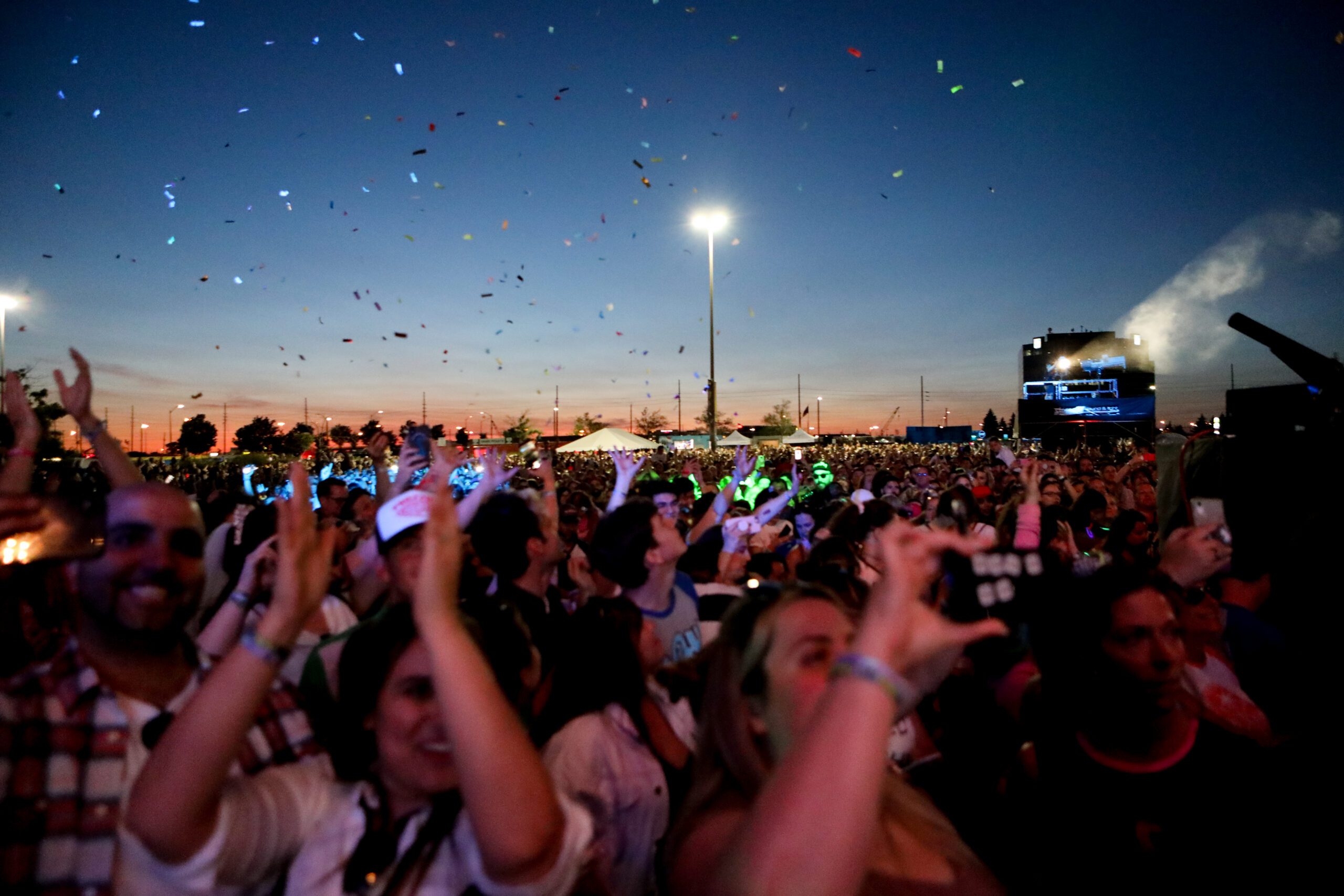 Image of a crowd at a concert with a sunset in the background and confetti falling