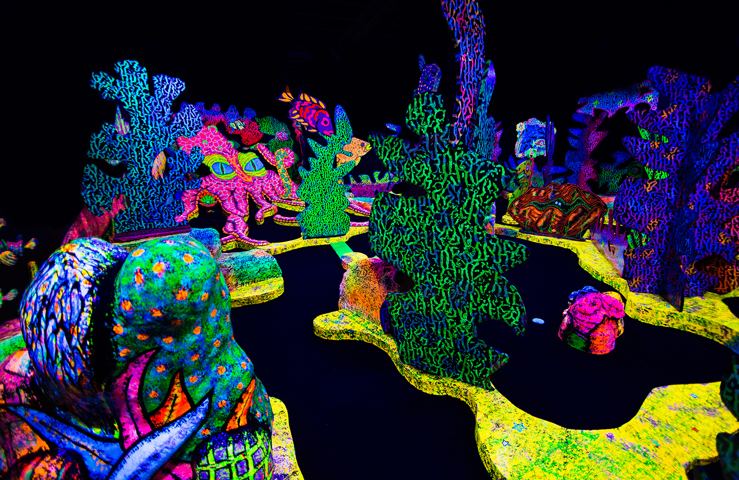 Image of an indoor mini-putt course that is decorated with glow-in-the-dark paint which glows under a black light