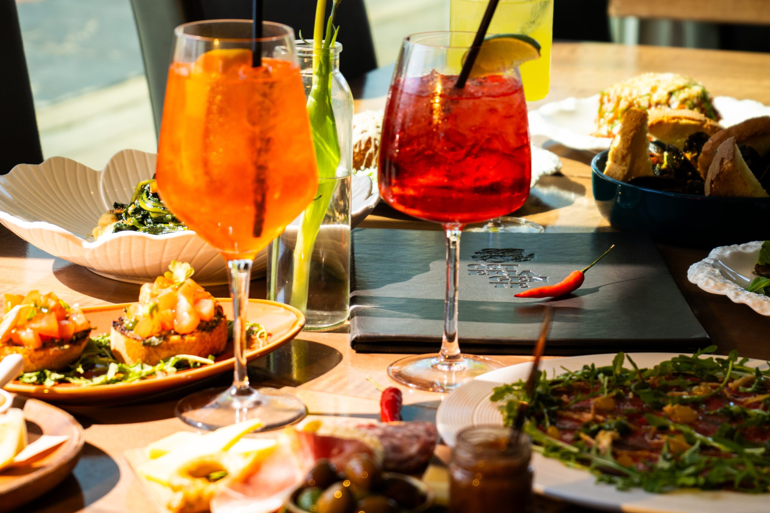 Image of a table in a restaurant full of plates of food and colourful cocktails