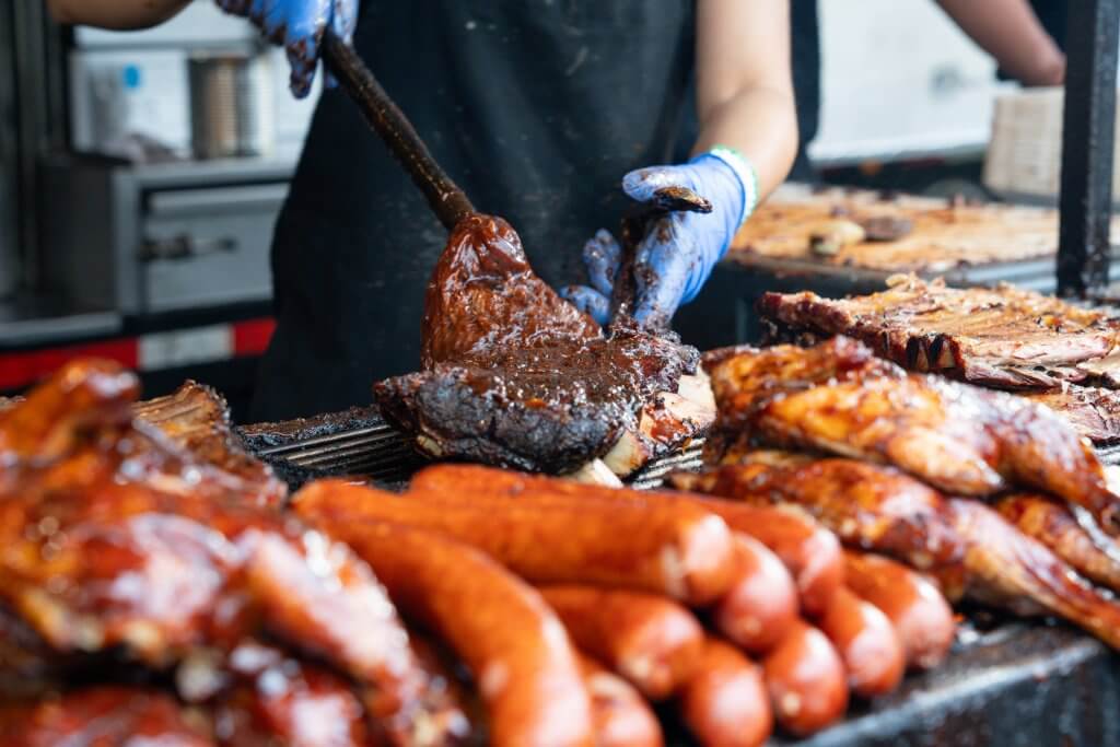 Image of a person standing behind a huge grill, cooking various meats