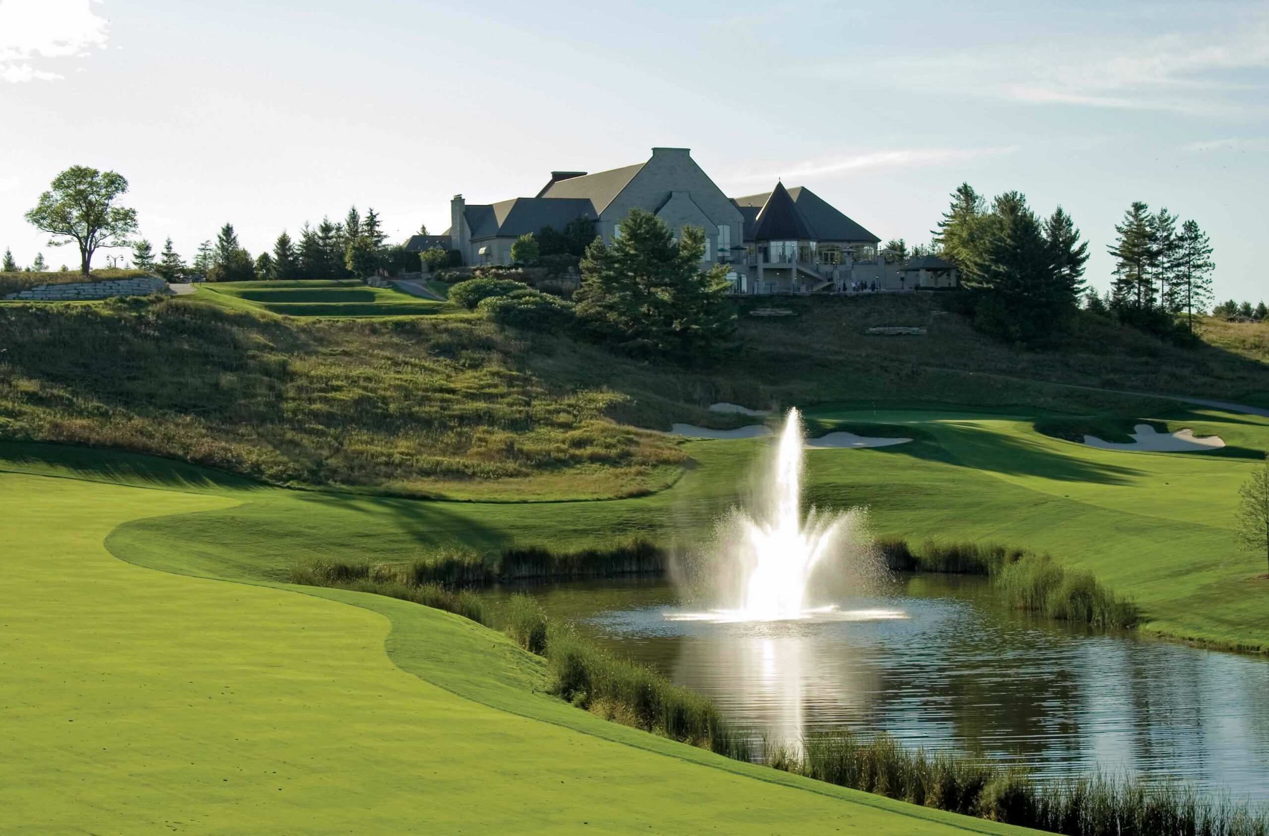 Image of a golf course's club house set behind a pond with a fountain in the center