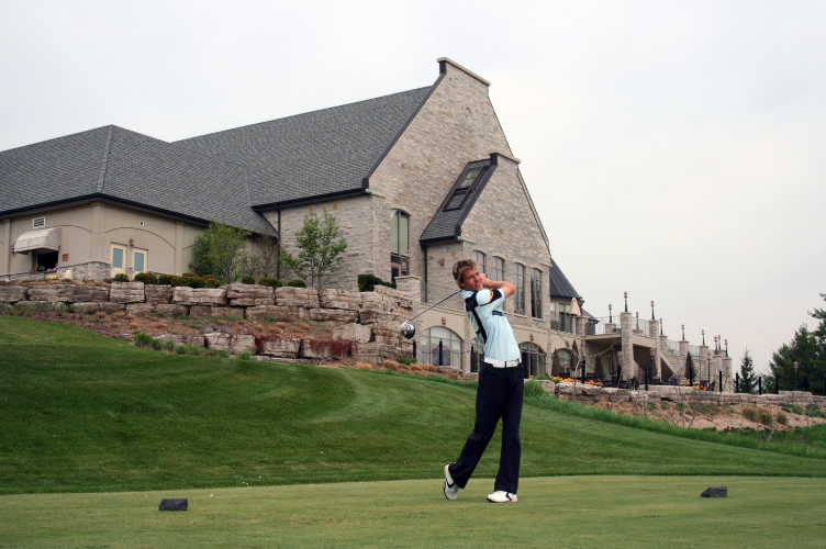 Image of a person swinging a golf club in from of a clubhouse
