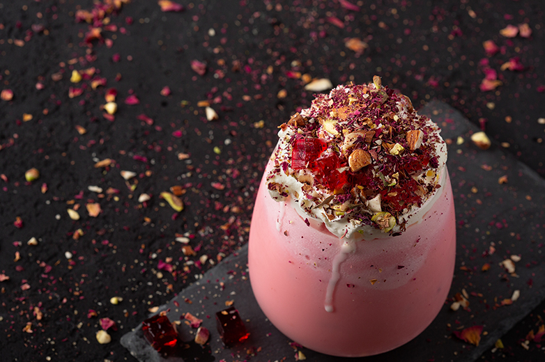 Image of a pink tea drink topped with rose petals and pistachios